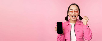 兴奋亚洲女孩笑着说微笑显示移动电话屏幕智能手机应用程序站粉红色的背景