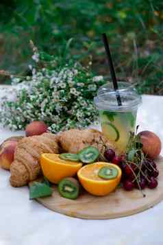 健康的野餐夏天一天羊角面包新鲜的水果柠檬水桃子樱桃猕猴桃橙子白色野花