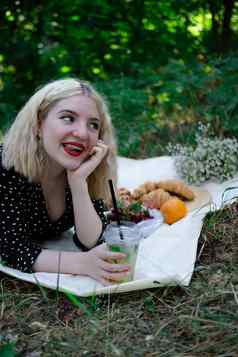 迷人的金发女郎年轻的女人野餐格子公园美味的零食柠檬水水果羊角面包夏季休息放松享受自由