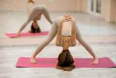 年轻的女人瑜伽健身房女孩长头发米色运动服站普拉萨里塔帕多塔纳萨那构成粉红色的地毯女人执行普拉萨里塔帕多塔纳萨那