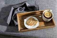 白色杯茶柠檬长白铜勺子扭曲的处理飞碟燕麦片饼干早餐木托盘破布餐巾灰色的沙发