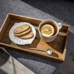 白色杯茶柠檬长白铜勺子扭曲的处理飞碟燕麦片饼干早餐木托盘破布餐巾灰色的沙发