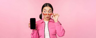 时尚的朝鲜文女孩年轻的女人太阳镜显示智能<strong>手机</strong>屏幕移动电话应用程序接口网站站粉红色的背景