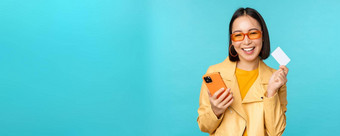 在线购物时尚的年轻的亚洲女人太阳镜显示信贷卡智能<strong>手机</strong>支付互联网使购买站蓝色的背景
