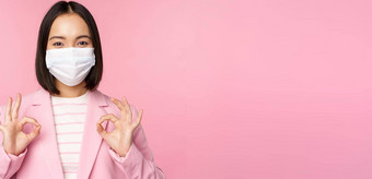 亚洲女商人西装医疗脸面具显示标志推荐保护设备办公室科维德流感大流行粉红色的背景