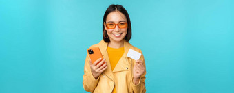 在线购物时尚的年轻的亚洲女人太阳镜显示信贷卡智能<strong>手机支付</strong>互联网使购买站蓝色的背景