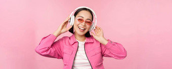 跳舞时尚的亚洲女孩听音乐耳机摆姿势粉红色的背景