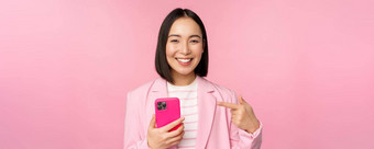 肖像微笑亚洲女商人指出移动电话推荐智能手机应用程序应用程序手机站粉红色的背景
