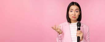 优柔寡断紧张亚洲业务女人持有小耸笨站麦克风粉红色的背景穿西装