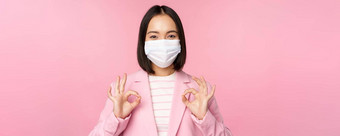 亚洲女商人西装医疗脸面具显示<strong>标志推荐</strong>保护设备办公室科维德流感大流行粉红色的背景