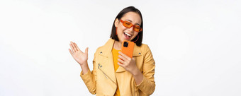 技术人概念快乐跳舞亚洲女孩太阳镜智能手机唱歌微笑站白色背景