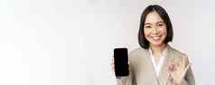 微笑亚洲女人显示智能手机屏幕标志企业人演示了移动电话应用程序接口站白色背景
