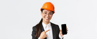 特写镜头微笑专业女亚洲建设工程师架构师西装安<strong>全面</strong>具介绍应用程序指出手指智能手机显示白色背景