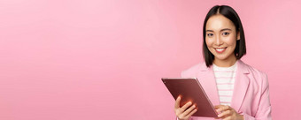 肖像年轻的亚洲企业女人办公室夫人数字平板电脑穿西装微笑专业摆姿势粉红色的背景