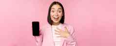 惊讶热情的亚洲女商人显示移动电话屏幕智能手机应用程序接口站粉红色的背景