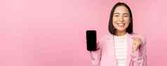 赢得朝鲜文女商人显示智能手机屏幕微笑很高兴展示移动电话应用程序在线商店购物应用程序站粉红色的背景