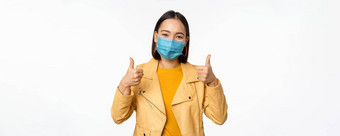 微笑亚洲女人医疗脸面具显示拇指支持穿保护设备科维德冠状病毒流感大流行白色背景