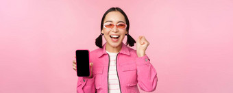 兴奋亚洲女孩笑着说微笑显示移动电话屏幕智能<strong>手机</strong>应用程序站粉红色的背景