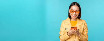 微笑亚洲女孩太阳镜智能手机应用程序持有移动电话站蓝色的背景