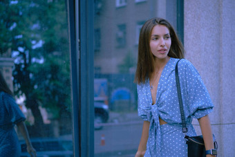 金发女郎女孩长蓝色的衣服小黑色的手提包肩膀摆姿势玻璃通过走城市时尚特写镜头