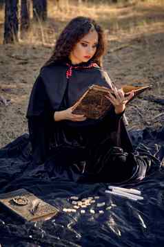 女巫黑色的衣服角罩摆姿势松森林坐着黑暗毯子呵呵书蜡烛符文完整的长度