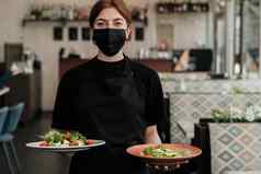 肖像年轻的女服务员穿保护面具持有盘子新鲜的沙拉餐厅