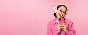 时尚的亚洲女孩耳机听音乐采取照片移动电话智能<strong>手机</strong>站粉红色的背景