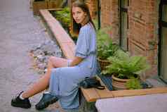 金发女郎女孩长蓝色的衣服小黑色的手提包肩膀摆姿势坐着横盘整理栏杆时尚风格完整的长度拍摄