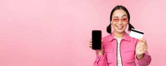 图像微笑朝鲜文女人显示信贷卡移动电话屏幕智能手机应用程序接口支付在线购物非接触式站粉红色的背景