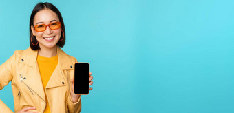 图像年轻的时尚的亚洲女模型时尚的太阳镜显示移动电话屏幕应用程序智能<strong>手机</strong>接口站蓝色的背景