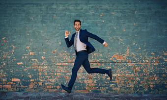 急切的成功肖像年轻的企业商人跳半空中砖墙