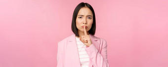 嘘禁忌概念肖像亚洲女商人显示嘘手势嘘标志新闻手指嘴唇站粉红色的背景西装