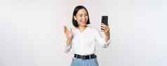 图像时尚的现代亚洲女人挥舞着手智能手机前面相机视频闲谈，聊天聊天人移动电话应用程序白色背景