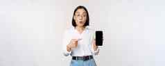 热情的年轻的亚洲女人指出手指智能手机屏幕显示广告移动电话白色背景
