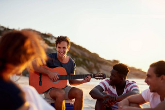 朋友<strong>激励激励</strong>拍摄男人。玩吉他坐着海滩朋友