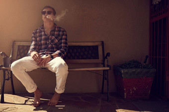 泡芙玄关拍摄年轻的男人。坐着板凳上吸烟香烟