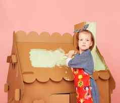 年轻的女孩绘画大纸板房子粉红色的背景