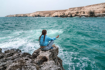 女人蓝色的夹克坐在岩石悬崖海狂风暴雨的海洋女孩旅行者休息认为梦想享受自然和平平静景观多风的天气