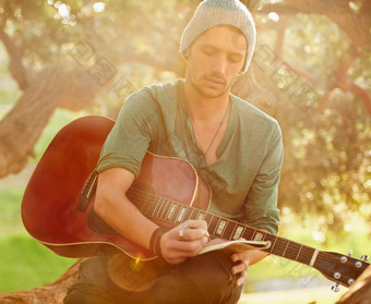 歌词启发自然拍摄英俊的年轻的男人。坐着公园吉他写作首歌记事本