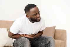 黑色的男人。腹部疼痛痛苦痛苦的腹部抽筋胃坐着沙发上首页腹部疼痛胃炎症阑尾炎概念