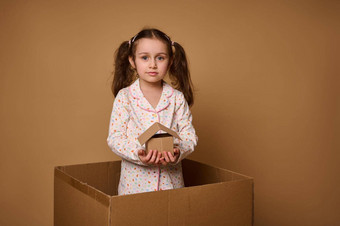 欧洲女孩可爱的孩子睡衣持有工艺纸板房子模型内部盒子米色背景复制空间广告概念投资住房