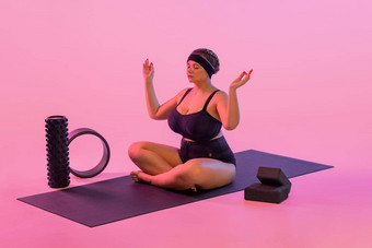 瑜伽肖像脂肪年轻的女人练习健身室内美丽的大小模型实践体式类冷静放松粉红色的背景