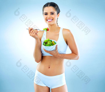 不要<strong>吃吃</strong>工作室肖像有吸引力的年轻的女人吃沙拉蓝色的背景
