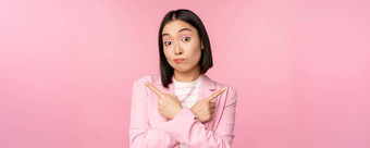 决定概念年轻的亚洲女商人企业工人指出手指sidways方向显示变体优柔寡断选择粉红色的背景