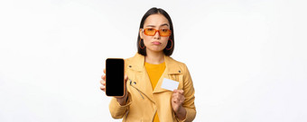 伤心亚洲女孩太阳镜显示智能手机应用程序接口信贷卡失望站白色背景