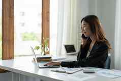 亚洲女商人会说话的移动电话工作移动PC金融现代办公室