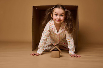 美丽的孩子女孩窥视纸板盒子相机工艺纸箱盒子米色背景复制空间广告住房保险真正的房地产概念