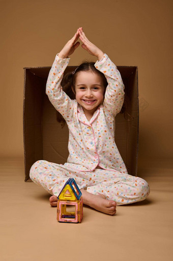 美丽的孩子持有手头形状房子屋顶坐在<strong>内部</strong>纸板盒子建筑房子磁<strong>构造</strong>函数微笑相机米色背景