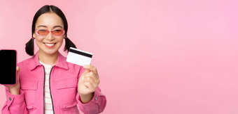 图像微笑朝鲜文女人显示信贷卡移动电话屏幕智能手机应用程序接口支付在线购物<strong>非接触</strong>式站粉红色的背景