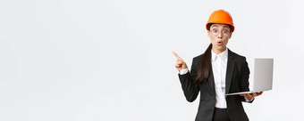 深刻的印象亚洲女企业家工厂穿安全头盔业务西装指出手指左持有移动PC电脑显示图企业白色背景